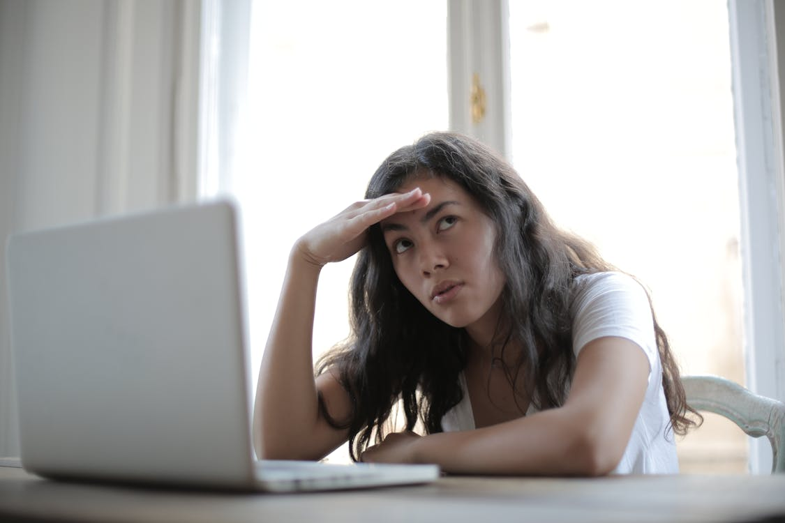 An immigrant with their laptop looking up and thinking